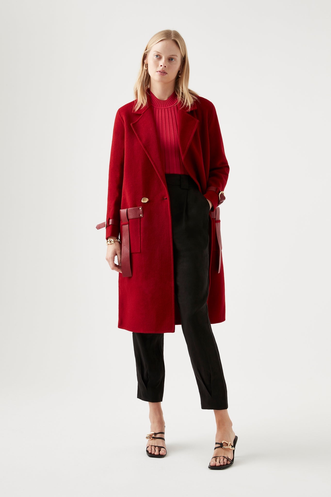 Woman wearing Aje Kingston Coat in dark red colour, a wool coat with double-breasted closure, accentuated with faux leather trims at the pockets and cuffs, which are adorned with gold buckle belts and gold buttons.